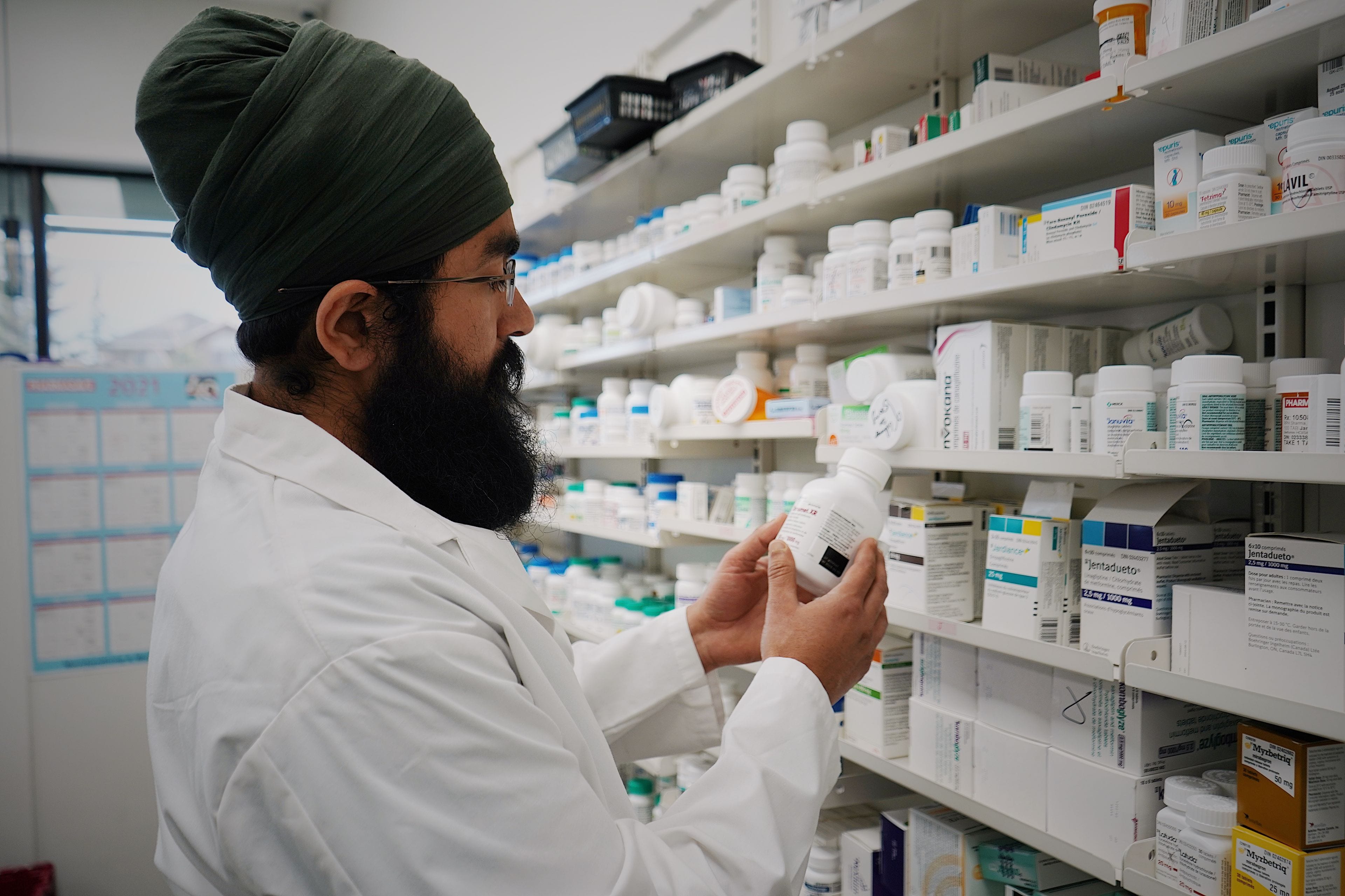 A pharmacist checking a medicine bottle against a wall of stock in a dispensary